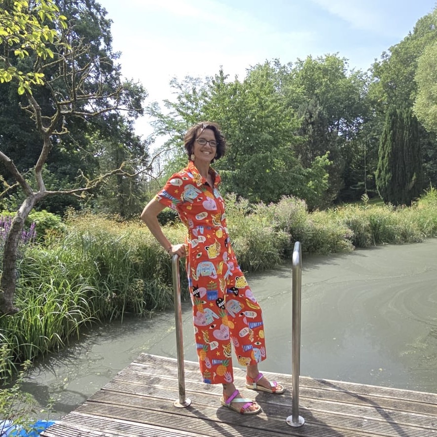 Pip Raine standing by a pond in a bright red patterned jumpsuit